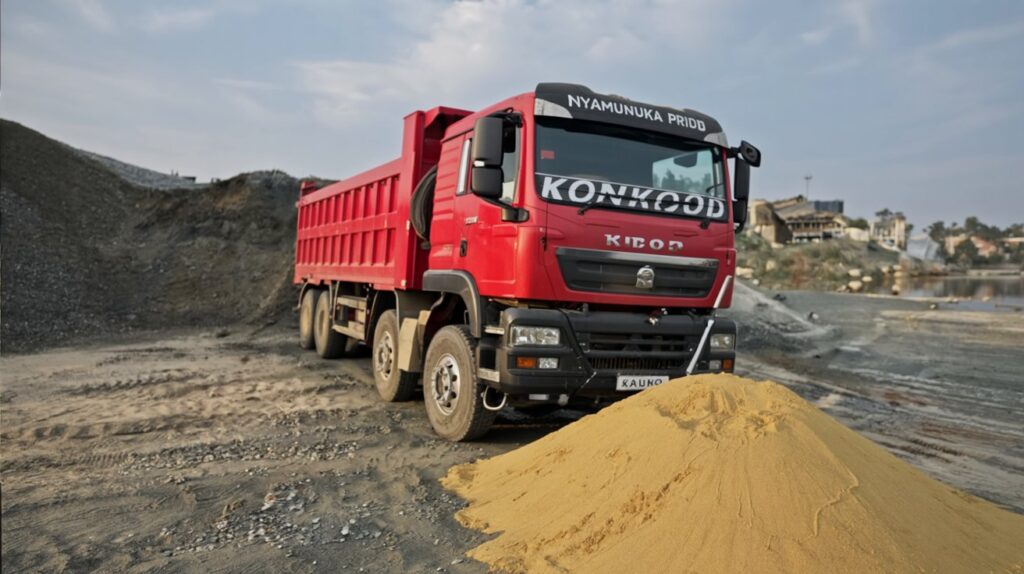 Yellow lake sand pile by Lake Victoria with a Konkood Sino truck and dredging boat in the background.